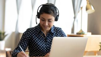 Étudiante porte un casque d'écoute assise devant portable et prend des notes