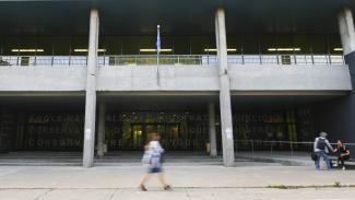 façade du campus de Montréal, femme en floue au centre de la photo et deux personnes à droite se serrant la main
