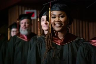 Étudiante souriante de l'ENAP à la collation des grades au premier plan, autres étudiants à l'arrière