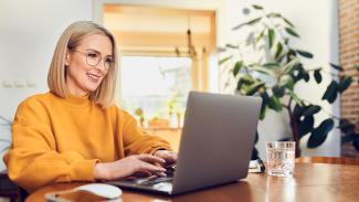  femme souriante d'âge moyen assise à la table avec un ordinateur portable et étudiant à la maison