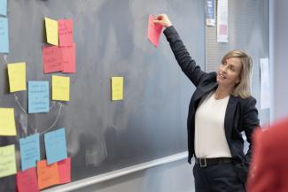 Femme souriante plaçant des papiers au Trello illustrant l'agilité et la planification