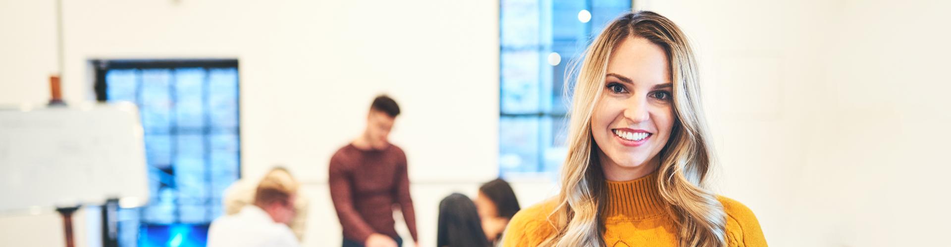 Femem souriante à l'avant-plan et collègues au travail en arrière